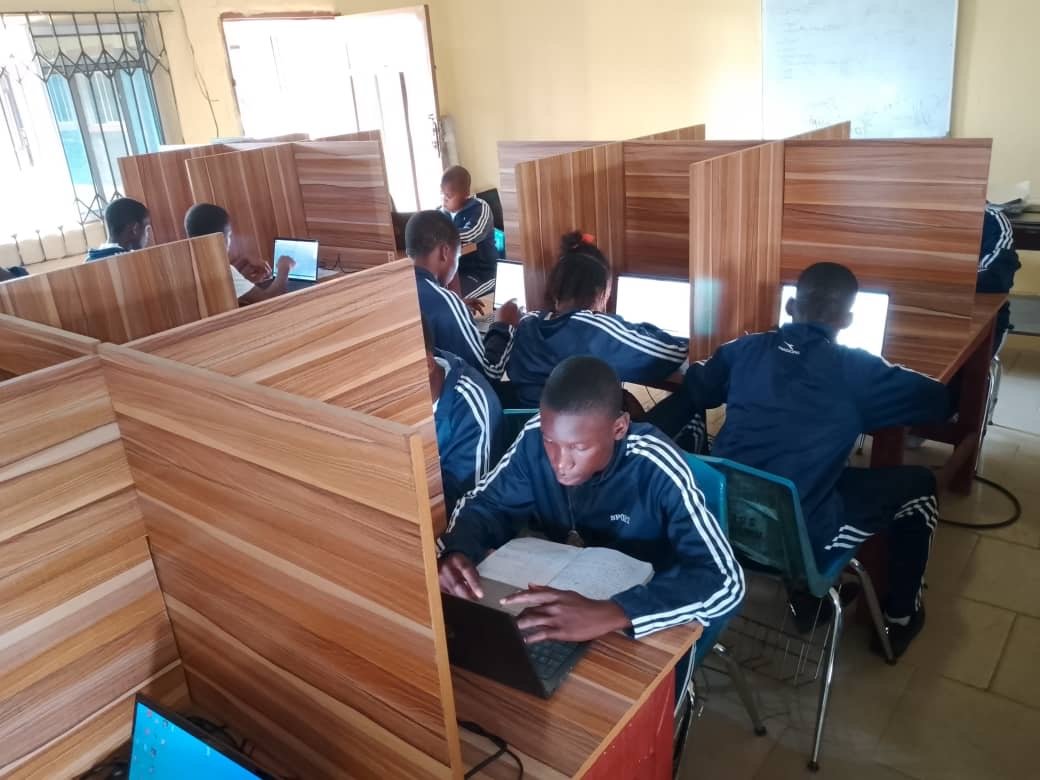 A young person at a laptop with an open exercise book alongside.